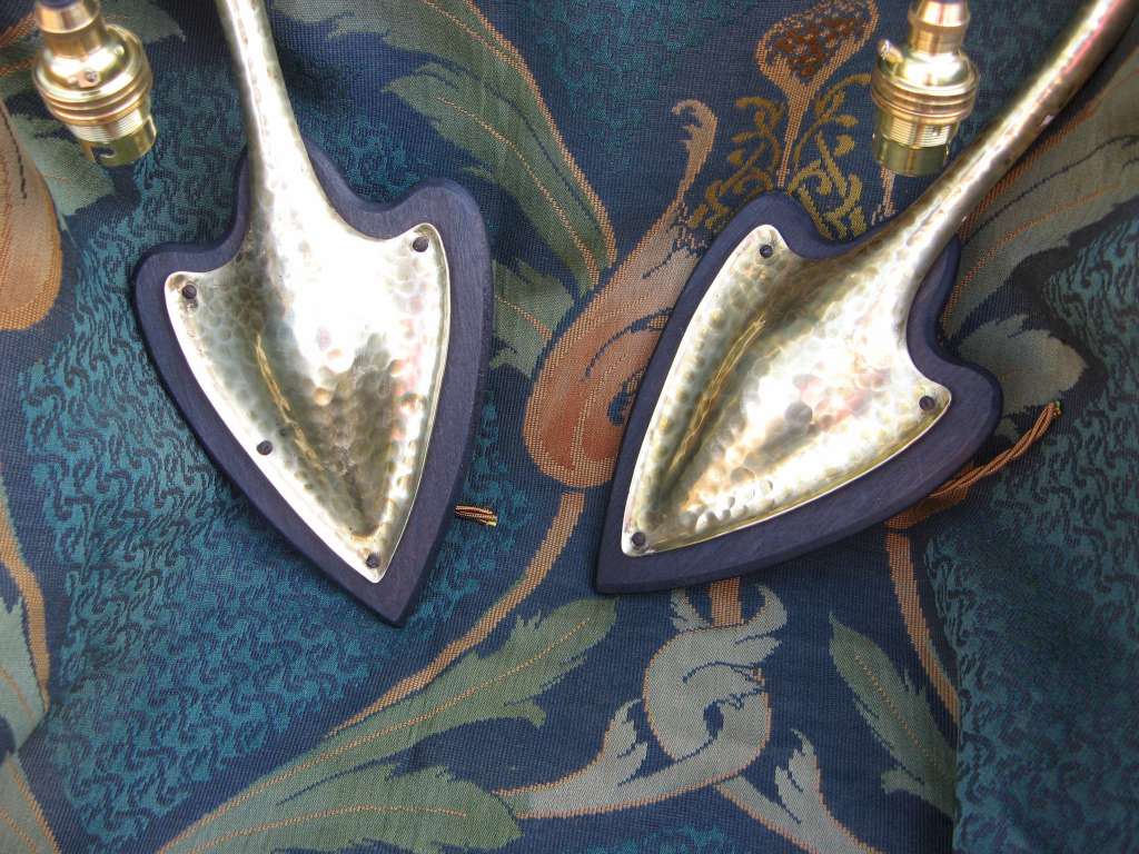 Pair of arts and crafts wall lights in hammered brass on wooden heart shaped back